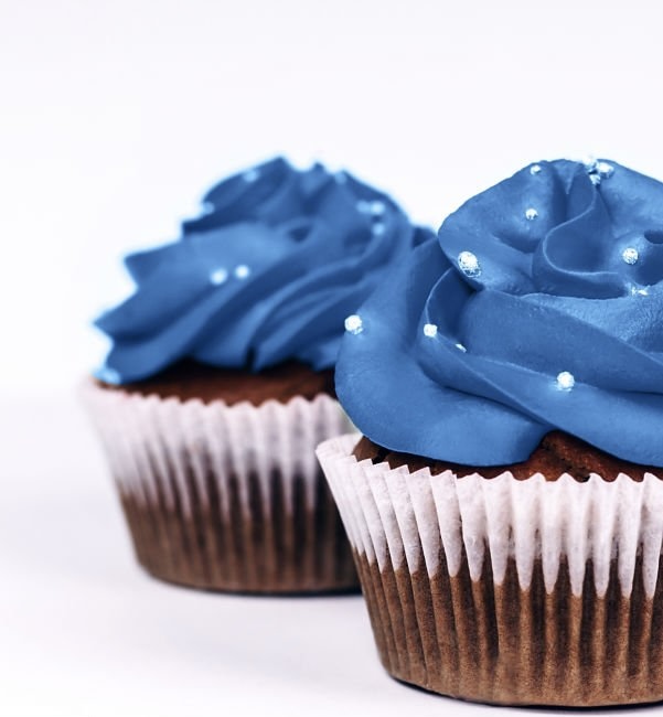 Three delicious cupcakes with icing in trendy blue color on isolated white background. Color of the year 2020 concept. Close-up.